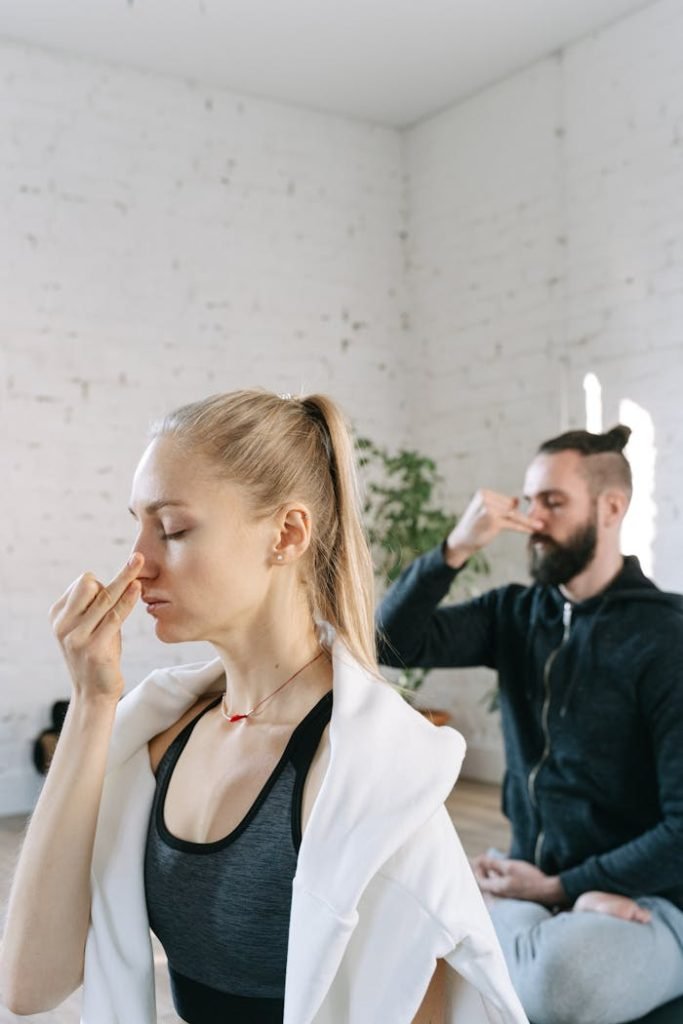 A man and woman perform breathing exercises in a serene indoor yoga session.