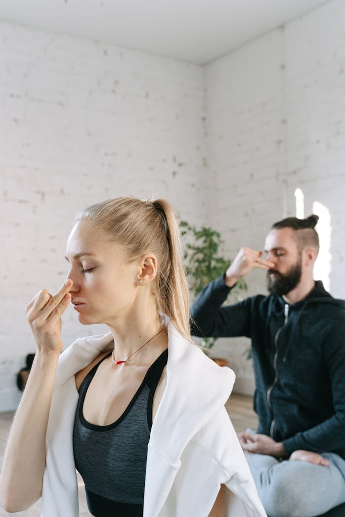 A man and woman perform breathing exercises in a serene indoor yoga session.