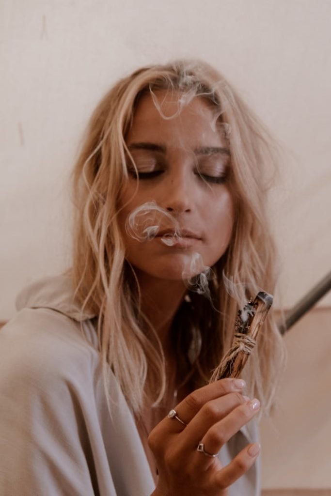 A serene woman meditating with incense, eyes closed, enjoying peaceful relaxation indoors.